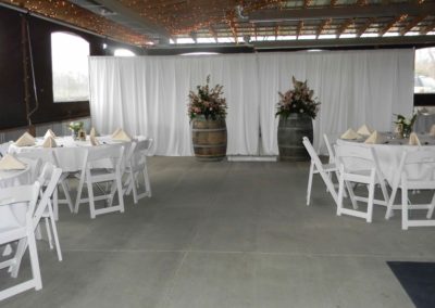 Marvel at the perfectly aligned rows of pristine white chairs, elegantly arranged on either side of the aisle, ready to honor and celebrate the bride and groom's parties. The natural light streaming through the event barn highlights the significance of this special gathering at Equus Run Vineyards.